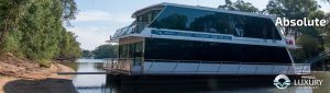 Luxury houseboat on a river near a wooded shore.