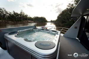 Hot tub on a houseboat deck overlooking a river with trees.